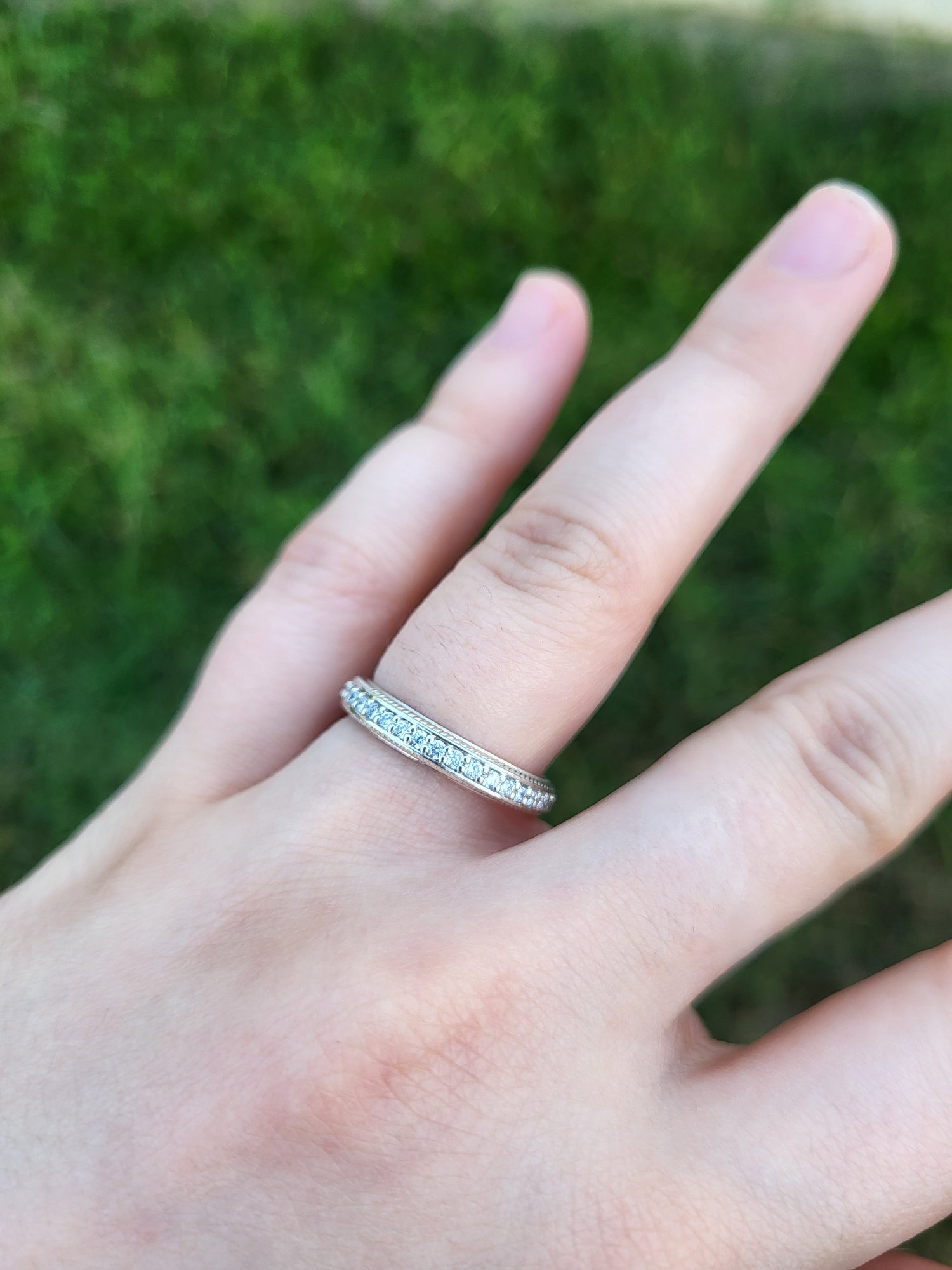 Hand wearing a silver diamond ring with small stones against a blurred green background