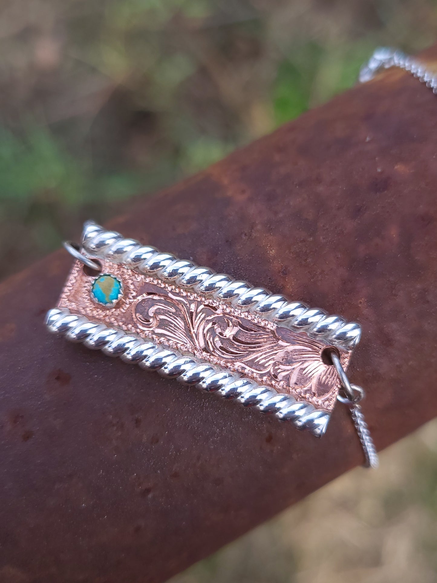Decorative pendant with intricate patterns and a turquoise stone on a rusty metal surface.